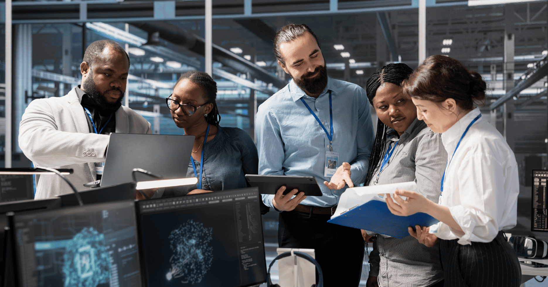 A diverse enterprise technology team collaborating around monitors displaying AI visualisations during an AI readiness assessment, reviewing findings on a tablet and printed documentation.